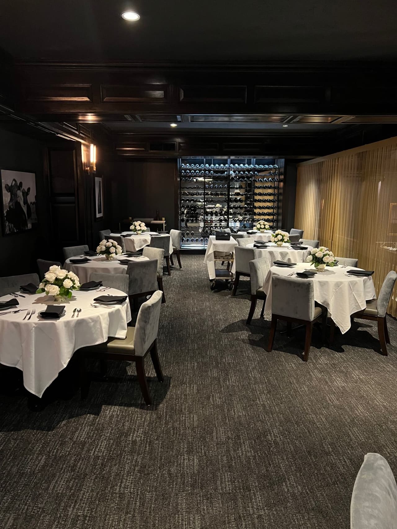 Round tables with white roses set Upstairs in front of the wine wall